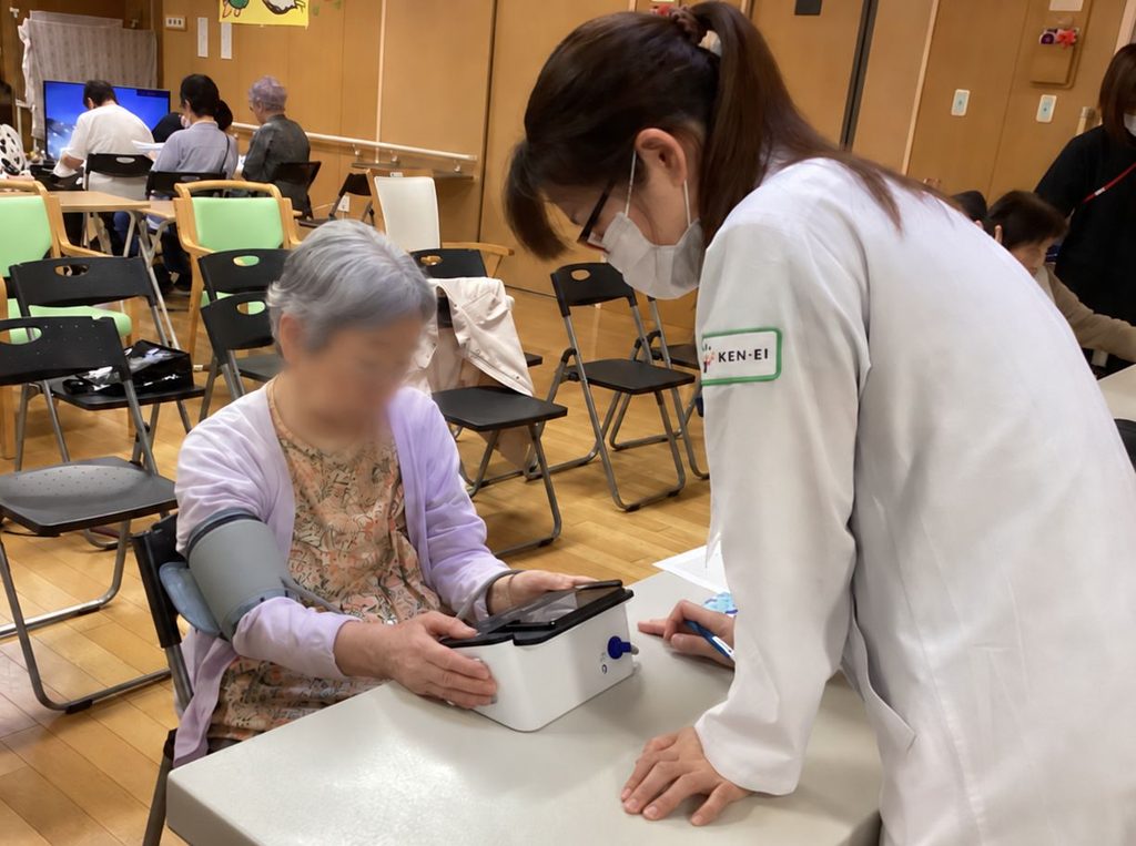 ファミリー薬局東陽町店の薬剤師が地域のグループホームの健康測定会で参加者の測定をサポートしている様子