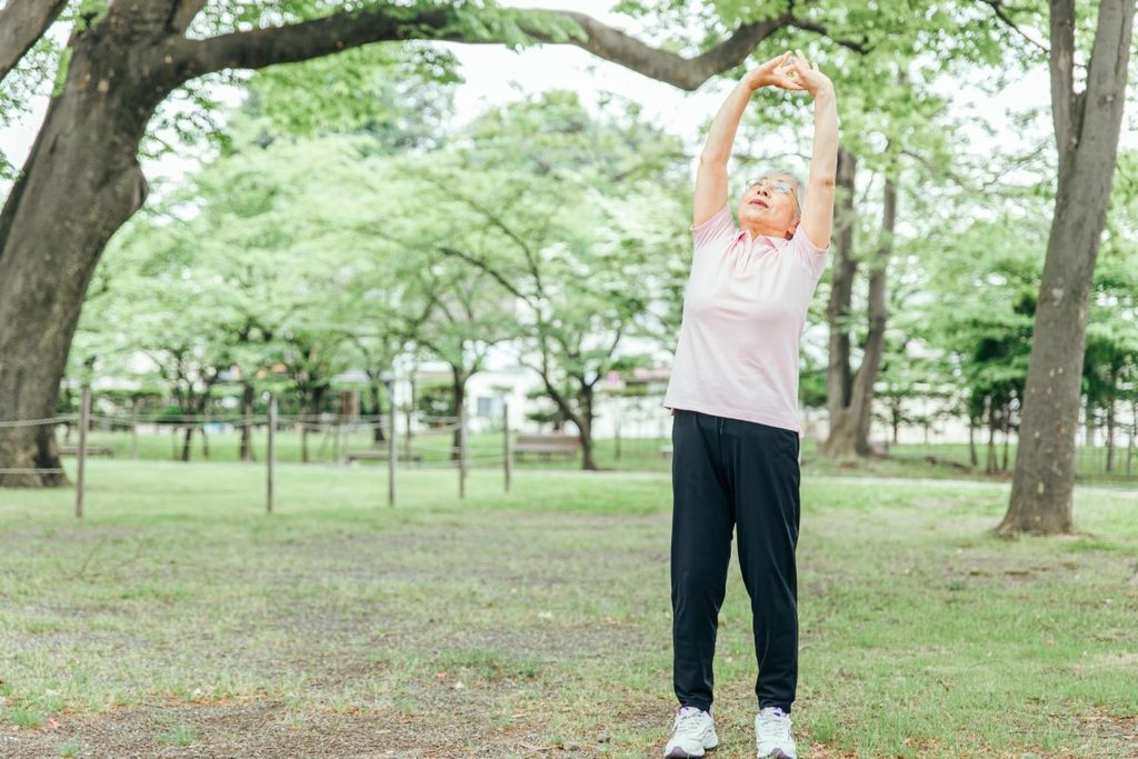 公園で両腕を上げて深呼吸する女性